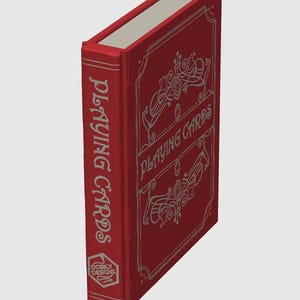 May include: A red playing card box with silver lettering and decorative flourishes. The spine reads "PLAYING CARDS" vertically. The front of the box also says "PLAYING CARDS" with decorative swirls. The bottom of the spine has a logo that says "DORKY DESIGNS".