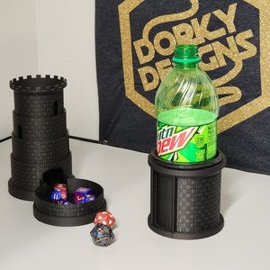 May include: Two black 3D printed towers with a brick pattern. One tower has a round opening at the bottom and is holding several dice. The other tower has a round opening at the top and is holding a green plastic bottle. The bottle has a white label with the text "Mountain Dew" on it. The towers are on a white surface.