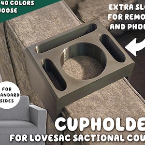 Puede incluir: Portavasos de plástico negro diseñado para un sofá seccional Lovesac. Tiene un portavasos grande y dos ranuras más pequeñas para mandos a distancia o teléfonos. El texto "EXTRA SLOTS FOR REMOTES AND PHONES" está impreso en la imagen.
