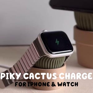 Może przedstawiać: Biały Apple Watch z różowym paskiem ładuje się na zielono-brązowej ładowarce w kształcie kaktusa. Ładowarka ma napis "SPIKY CACTUS CHARGER FOR IPHONE & WATCH".