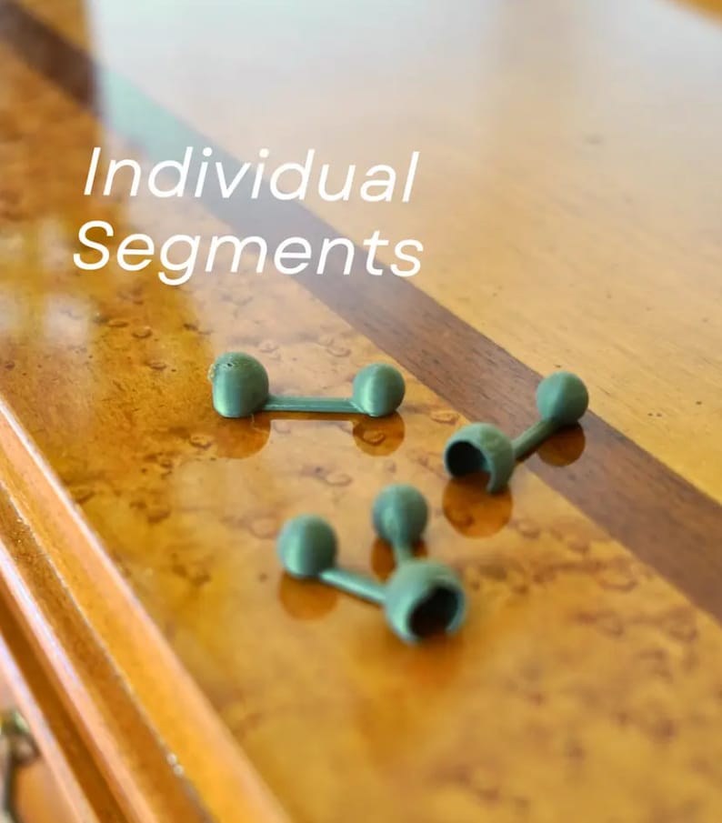 May include: Three green plastic connectors, each with two round ends, are arranged on a wooden surface. The text "Individual Segments" is visible above the connectors.