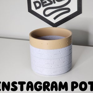 May include: A white ceramic planter with a light brown rim and a speckled texture. The planter has the text "INSTAGRAM POT" printed below it.