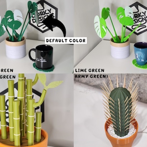 May include: Three different 3D printed plant designs in various shades of green. The first design is a monstera plant in a white pot. The second design is a bamboo plant in an orange pot. The third design is a cactus plant in an orange pot. The text "Dorky Designs" is visible in the background.