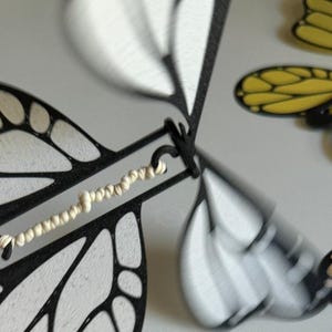 May include: A black and white butterfly wind-up toy with a white string attached to the wings. The toy is made of plastic and has a detailed design.