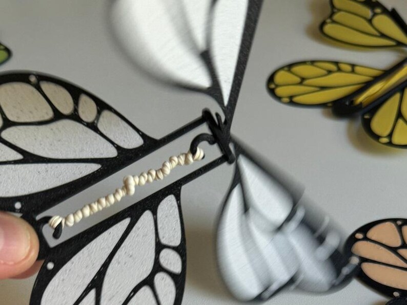 May include: A black and white butterfly wind-up toy with a white string attached to the wings. The toy is made of plastic and has a detailed design.