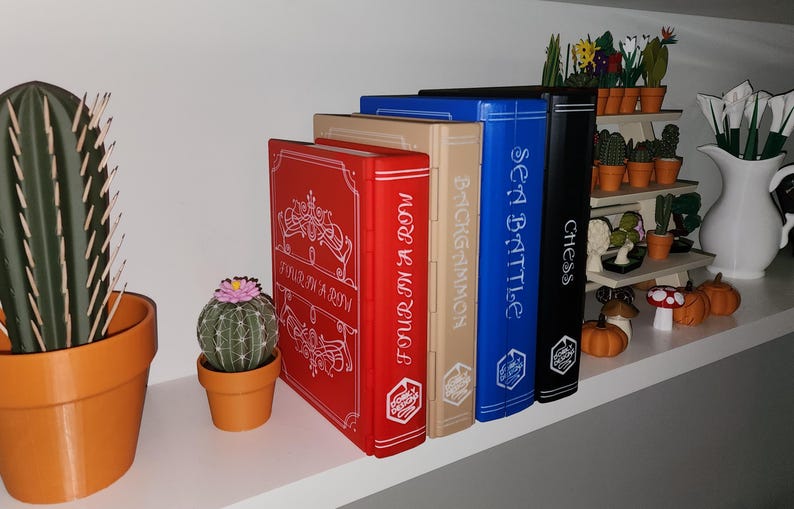 May include: A shelf displays decorative board game boxes labeled "Four in a Row," "Backgammon," "Sea Battle," and "Chess." A cactus and a small potted cactus are on the left. Miniature pumpkins and a white pitcher are on the right.