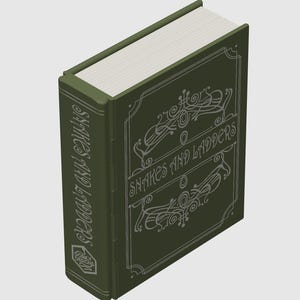 May include: A dark olive green book-shaped game box titled Snakes and Ladders. The cover features white decorative filigree lines and the title in a stylised font. The spine also displays the title and a small hexagonal Dorky Designs logo.
