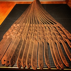 May include: A collection of brown leather guitar straps with a woven design. The straps are laid out in a fan shape on a black surface.