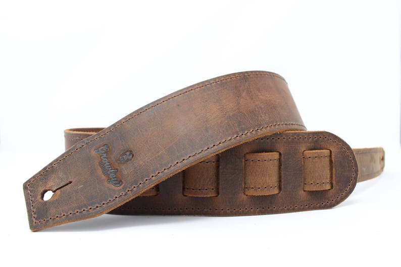 May include: Brown leather guitar strap with adjustable length and a stitched design. The strap has the word "Groundhog" embossed on it.