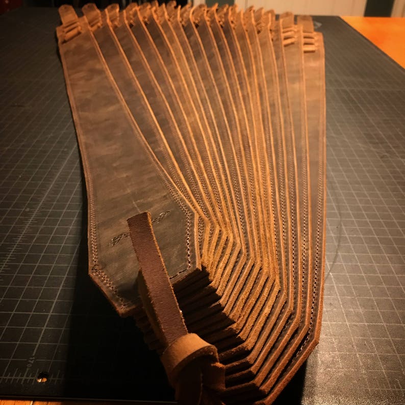 May include: A stack of brown leather straps, folded in a fan shape. The straps are stitched with a decorative pattern.