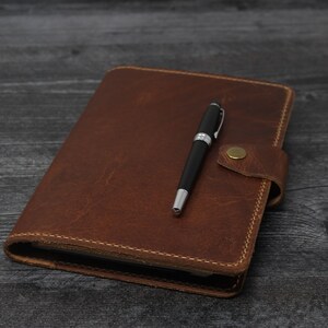 May include: A brown leather-bound journal with a pen on top of it.