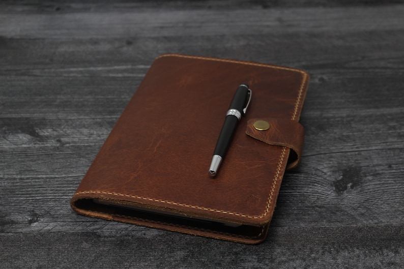 May include: A brown leather-bound journal with a pen on top of it.