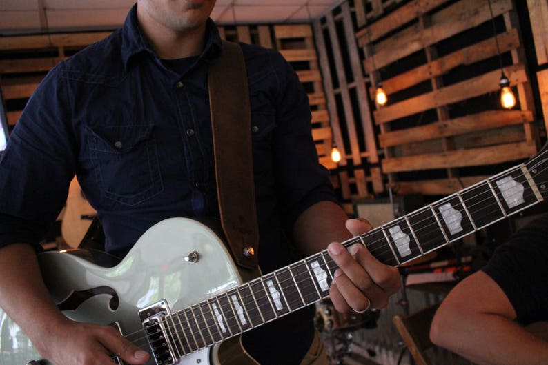 May include: A person playing a light blue electric guitar with a brown leather strap. The guitar has a white pickguard and a black fretboard.