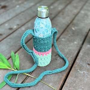 May include: A teal crochet water bottle holder with a matching strap. The holder has a green, pink, and light green color block design. A floral patterned water bottle with a silver lid is inside the holder.