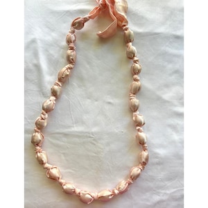May include: A pink satin necklace with knotted beads. The necklace is tied with a bow at the top.