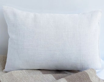 May include: A white linen pillow with a smooth, textured surface. The pillow is lying on a brown and beige striped blanket.
