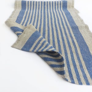 Könnte beinhalten: Ein blauer und naturfarbener Tischläufer aus Leinen mit Streifen. Der Läufer ist in der Mitte gefaltet und die blauen Streifen sind sichtbar.