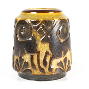 Puede incluir: Un jarrón cilíndrico de cerámica con un esmalte marrón oscuro y amarillo. El jarrón presenta un patrón repetido de ciervos estilizados y motivos florales. La parte superior e inferior tienen un color marrón más oscuro, mientras que la sección media tiene un tono amarillo más claro.