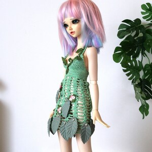 May include: A doll with pink and blue hair wearing a green crocheted dress with leaves and flowers. The dress is a halter style with a crochet design.