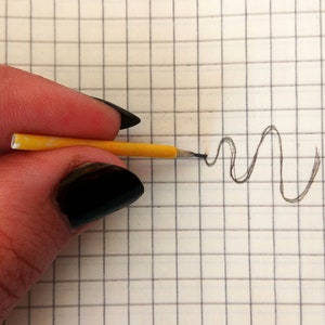 Puede incluir: Una mano sosteniendo un lápiz amarillo con una goma de borrar negra, dibujando una línea ondulada en una hoja de papel cuadriculado.