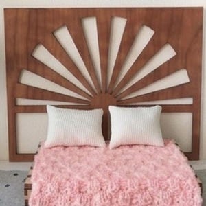 May include: Miniature bedroom scene with a wooden headboard, a pink fluffy blanket, and two white pillows. A small bonsai tree and a white bookshelf with decorative items complete the scene. The rug has a feather pattern.