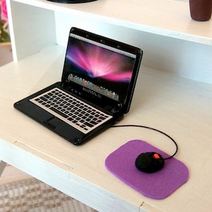 Könnte beinhalten: Weißer Schreibtisch mit einem Laptop, einem lila Mauspad und einer kabellosen Maus. Der Schreibtisch hat ein Regal über der Arbeitsfläche. Eine Topfpflanze steht auf dem Regal.