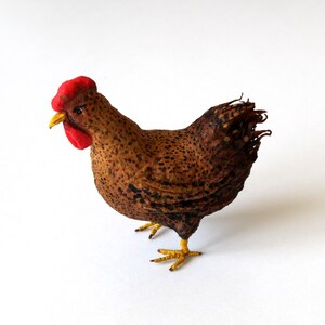May include: A brown and black speckled chicken figurine with a red comb and yellow feet. The chicken is standing on a white surface.
