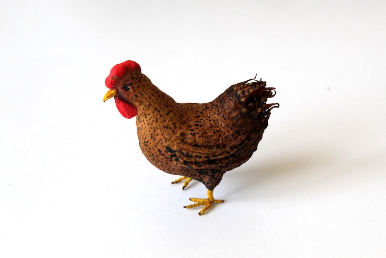May include: A brown and black speckled chicken figurine with a red comb and yellow feet. The chicken is standing on a white surface.