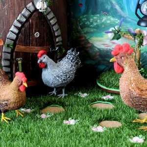May include: Three miniature chickens in a miniature garden setting. One chicken is gray and white, one is brown and white, and one is brown with black speckles. The chickens are standing on green grass with brown and white flowers.