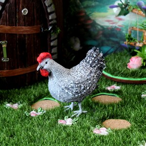 May include: A gray and white speckled chicken figurine with a red comb stands on a green grassy surface with small pink flowers. The chicken is facing the left side of the image.