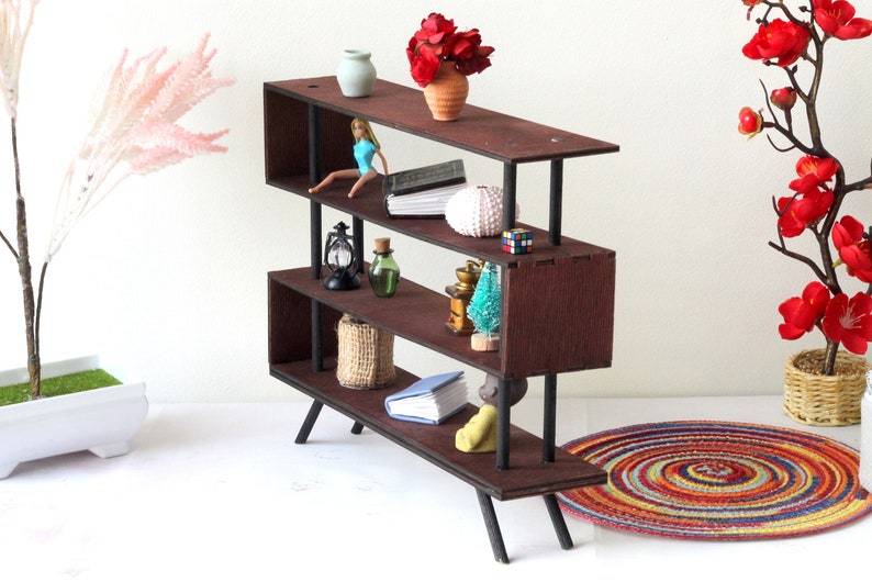 Puede incluir: Una estanter&iacute;a de madera de tres niveles con patas y soportes de metal negro. Las estanter&iacute;as est&aacute;n llenas de art&iacute;culos decorativos, incluyendo una mu&ntilde;eca, un libro, una concha, una linterna, una botella, una cesta, un &aacute;rbol peque&ntilde;o y un libro. La estanter&iacute;a est&aacute; sobre una superficie blanca con una alfombra colorida en primer plano.