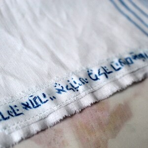 May include: A white fabric with blue stripes and a blue embroidered label that reads "ELE: NOLI:  GSL:  CND:  GSL"