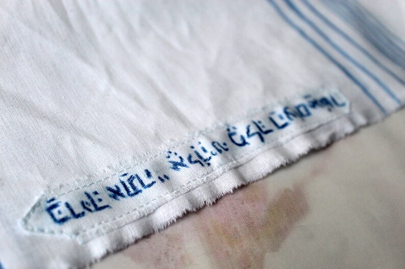 May include: A white fabric with blue stripes and a blue embroidered label that reads "ELE: NOLI:  GSL:  CND:  GSL"