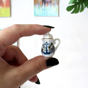 May include: A small, white porcelain teapot with a blue and gold floral design. The teapot has a lid and a handle.
