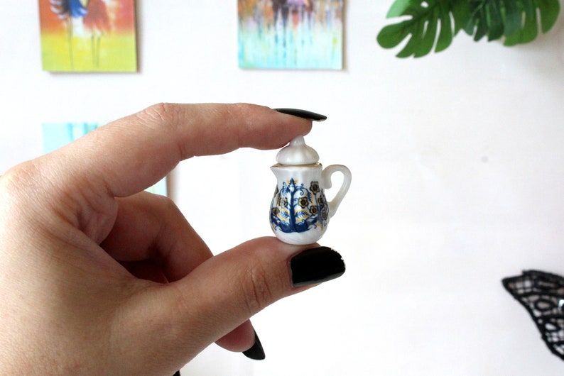 May include: A small, white porcelain teapot with a blue and gold floral design. The teapot has a lid and a handle.