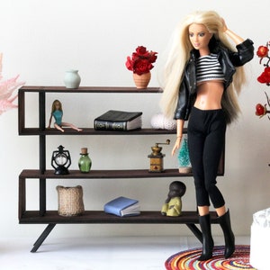 Puede incluir: Una estanter&iacute;a de metal negro con tres estantes, que presenta una variedad de art&iacute;culos decorativos, incluyendo una mu&ntilde;eca, un libro, una linterna, un jarr&oacute;n, una planta y un molinillo de caf&eacute;. La estanter&iacute;a est&aacute; contra una pared blanca.