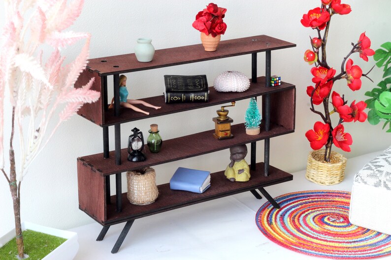 Puede incluir: Una estanter&iacute;a de madera marr&oacute;n con patas de metal negro y tres estantes. Los estantes est&aacute;n decorados con varios art&iacute;culos, incluyendo un libro, una mu&ntilde;eca, una linterna, una botella, un molinillo de caf&eacute;, un &aacute;rbol peque&ntilde;o, un erizo de mar, una peque&ntilde;a estatua y un libro azul. La estanter&iacute;a est&aacute; sobre una superficie blanca.