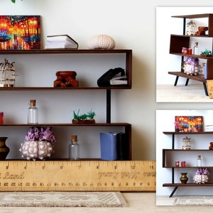 Puede incluir: Una estanter&iacute;a de madera en miniatura con cuatro estantes, que presenta una variedad de art&iacute;culos decorativos, incluyendo una jaula para p&aacute;jaros, una concha marina, un jarr&oacute;n y una pintura. La estanter&iacute;a est&aacute; hecha de madera marr&oacute;n oscura y tiene detalles met&aacute;licos negros. Una regla se coloca delante de la estanter&iacute;a, con el texto "Lenas Mini Land" impreso en ella.