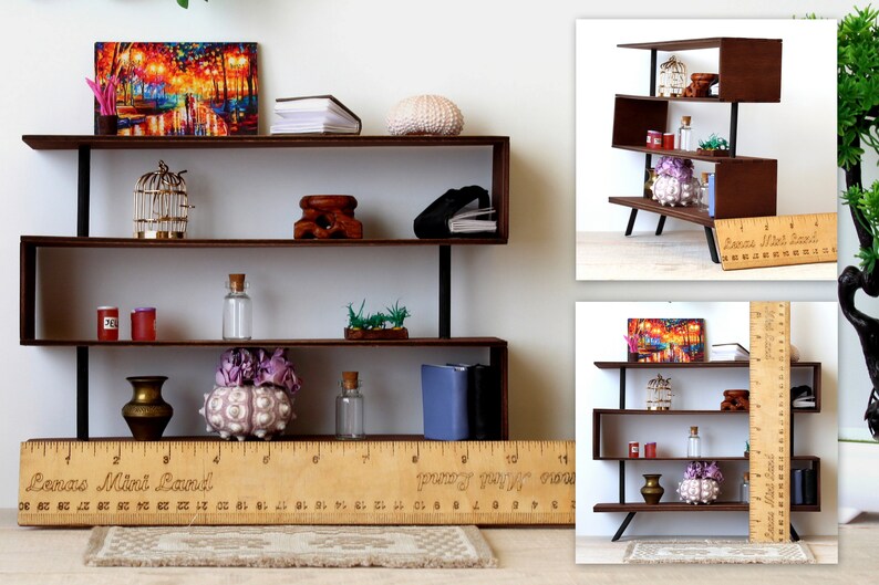 Puede incluir: Una estanter&iacute;a de madera en miniatura con cuatro estantes, que presenta una variedad de art&iacute;culos decorativos, incluyendo una jaula para p&aacute;jaros, una concha marina, un jarr&oacute;n y una pintura. La estanter&iacute;a est&aacute; hecha de madera marr&oacute;n oscura y tiene detalles met&aacute;licos negros. Una regla se coloca delante de la estanter&iacute;a, con el texto "Lenas Mini Land" impreso en ella.