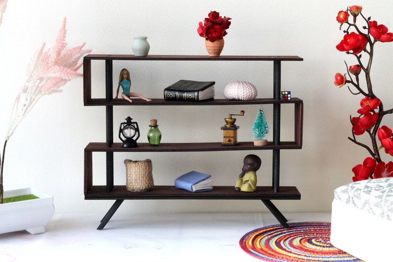 Puede incluir: Una estanter&iacute;a de madera de tres niveles con detalles en metal negro. Las estanter&iacute;as est&aacute;n llenas de varios art&iacute;culos decorativos, incluyendo una mu&ntilde;eca, un libro, una linterna, una botella, un molinillo de caf&eacute;, un &aacute;rbol peque&ntilde;o, un libro, una cesta y una peque&ntilde;a figurita. La estanter&iacute;a est&aacute; sobre una superficie blanca con una alfombra colorida en primer plano.