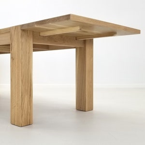 May include: A wooden dining table with a leaf extension. The table has a natural wood finish and four square legs.