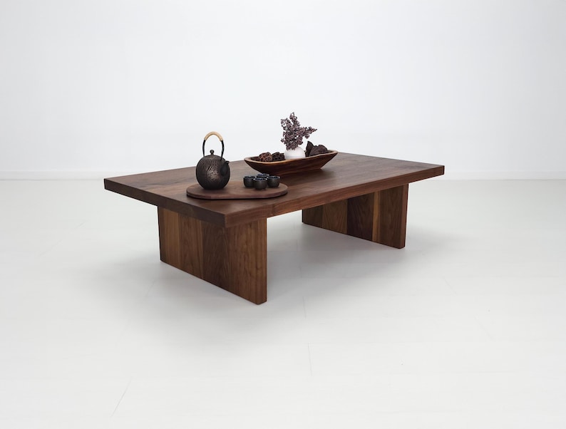 K&ouml;nnte beinhalten: Ein dunkler Holz-Couchtisch mit einer rechteckigen Tischplatte und vier Beinen. Der Tisch ist mit einer Teekanne, Tassen und einer Schale getrockneter Blumen dekoriert.
