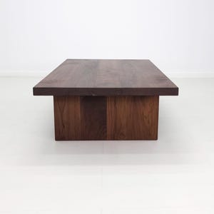 Solid walnut LILY coffee table with a thick slab top and panel legs, showcasing rich wood grain.