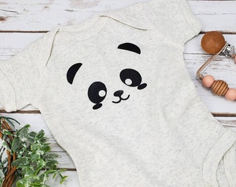 May include: A white baby onesie with a black panda face graphic. The panda has large eyes and a small nose and mouth.