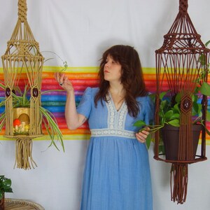 A woman in a long, vintage, sky blue dress stands between two  vintage-style handmade XL  plant hangers and tends to the plants they hold