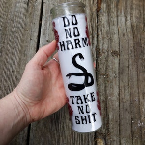 May include: White candle with a black snake design and the text "Do No Harm Take No Shit" in black lettering. The candle is decorated with red roses.