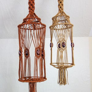 May include: Two macrame plant hangers with wooden beads. The hanger on the left is brown and the hanger on the right is beige.