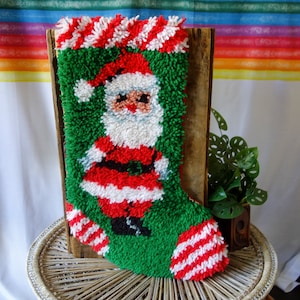 May include: A green and red Christmas stocking with a Santa Claus design. The stocking is made of yarn and has a fluffy texture.