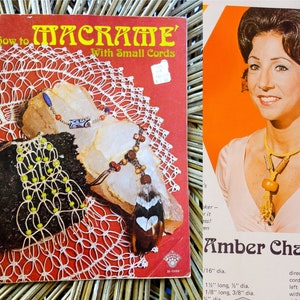 May include: A vintage book titled "How to Macrame with Small Cords" featuring a close-up of a white macrame doily with beads and a feather. The book cover is red with white text. The book is next to a photo of a woman with brown hair wearing a macrame necklace.