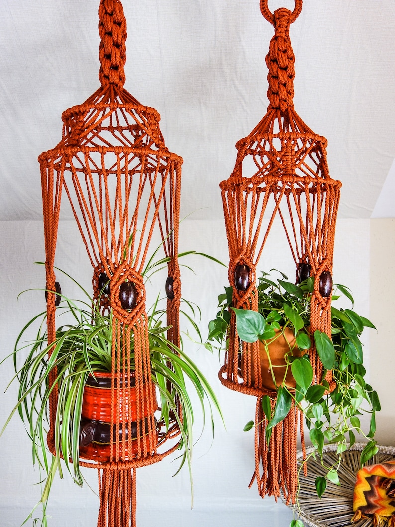May include: Two macrame plant hangers with wooden beads, each holding a potted plant. The hangers are made of brown cord and have a geometric design.